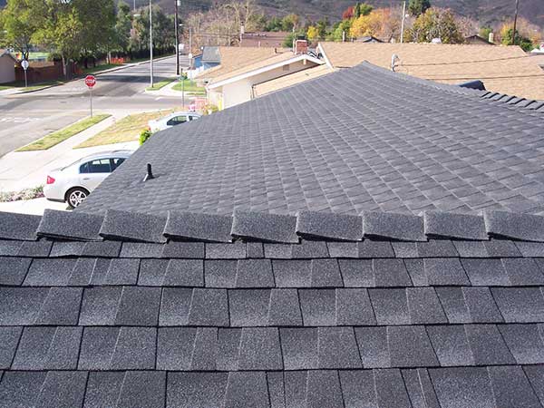 new dark gray asphalt roof shingle installation over ridge